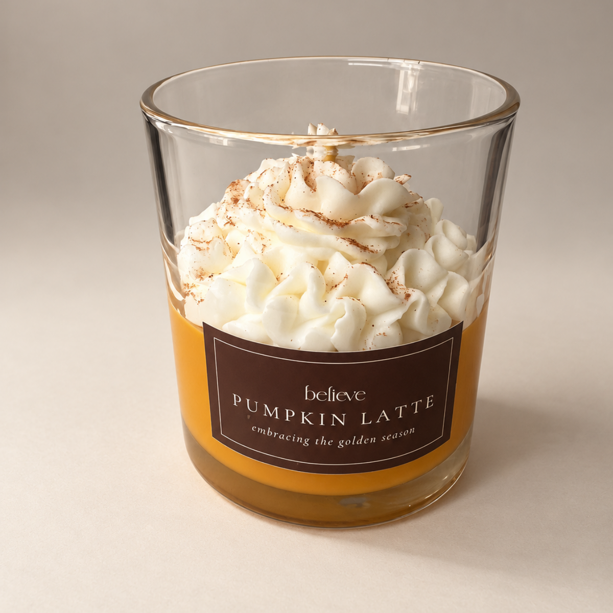 Pumpkin Latte candle against a soft neutral backdrop, showing the whipped wax top and the brown BELIEVE label