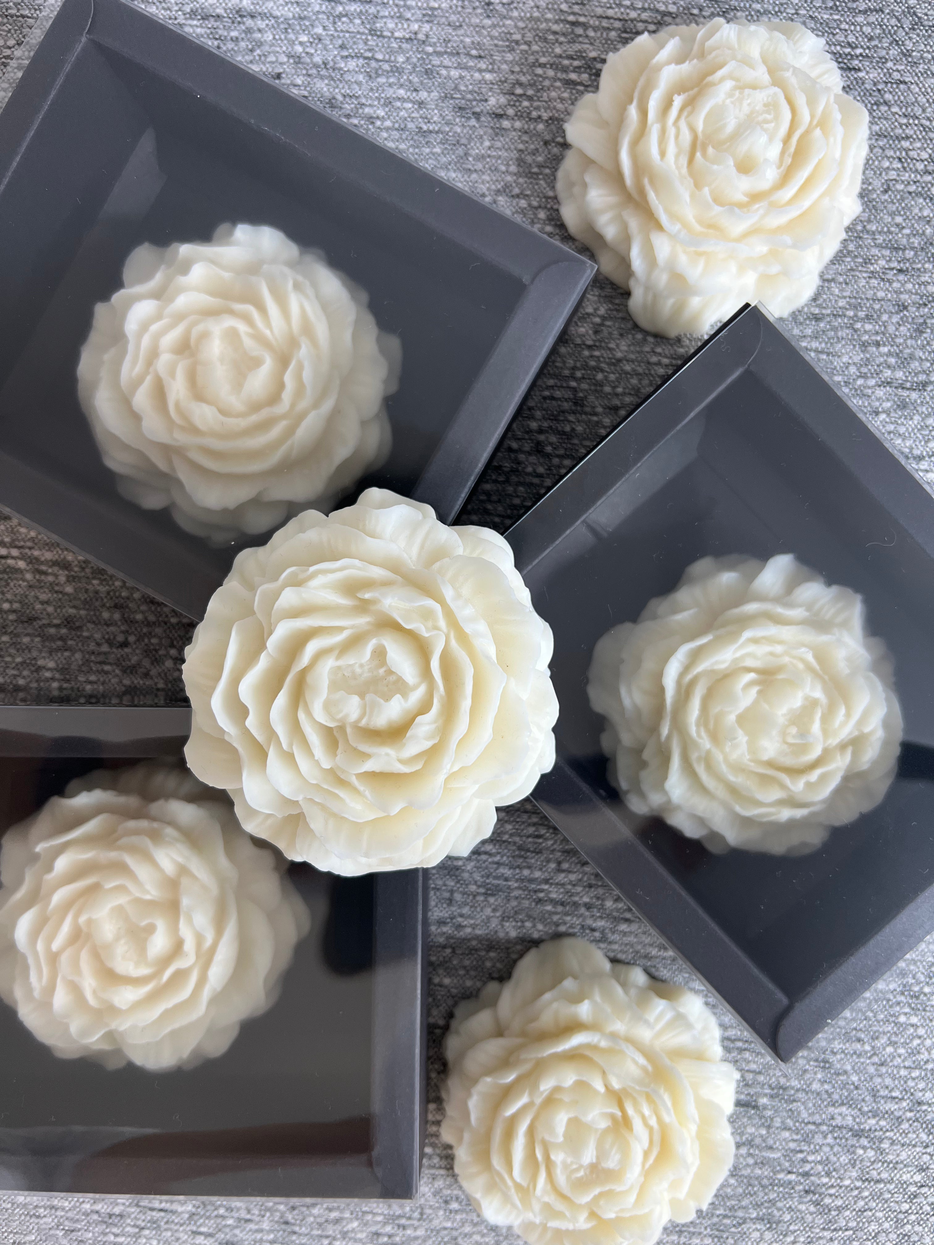 Cream flower-shaped BELIEVE candles arranged on dark grey gift boxes