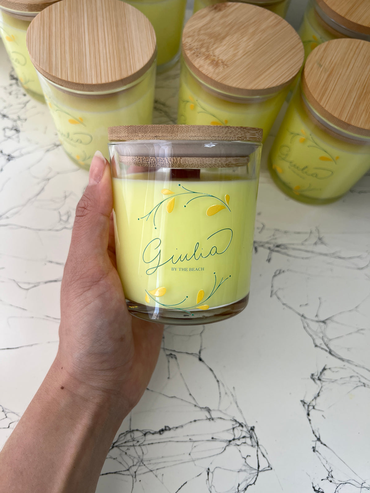 Hand holding a yellow custom-branded candle, with matching candles on the shelf behind