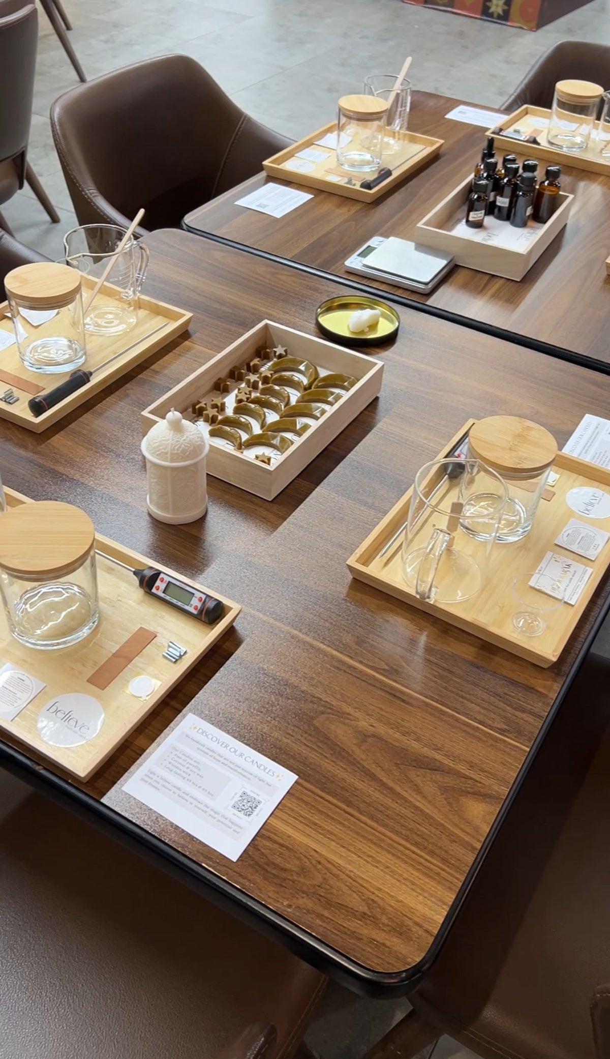 A BELIEVE candle making workshop table set with glass candle jars, bamboo trays, fragrance oils and wax pieces